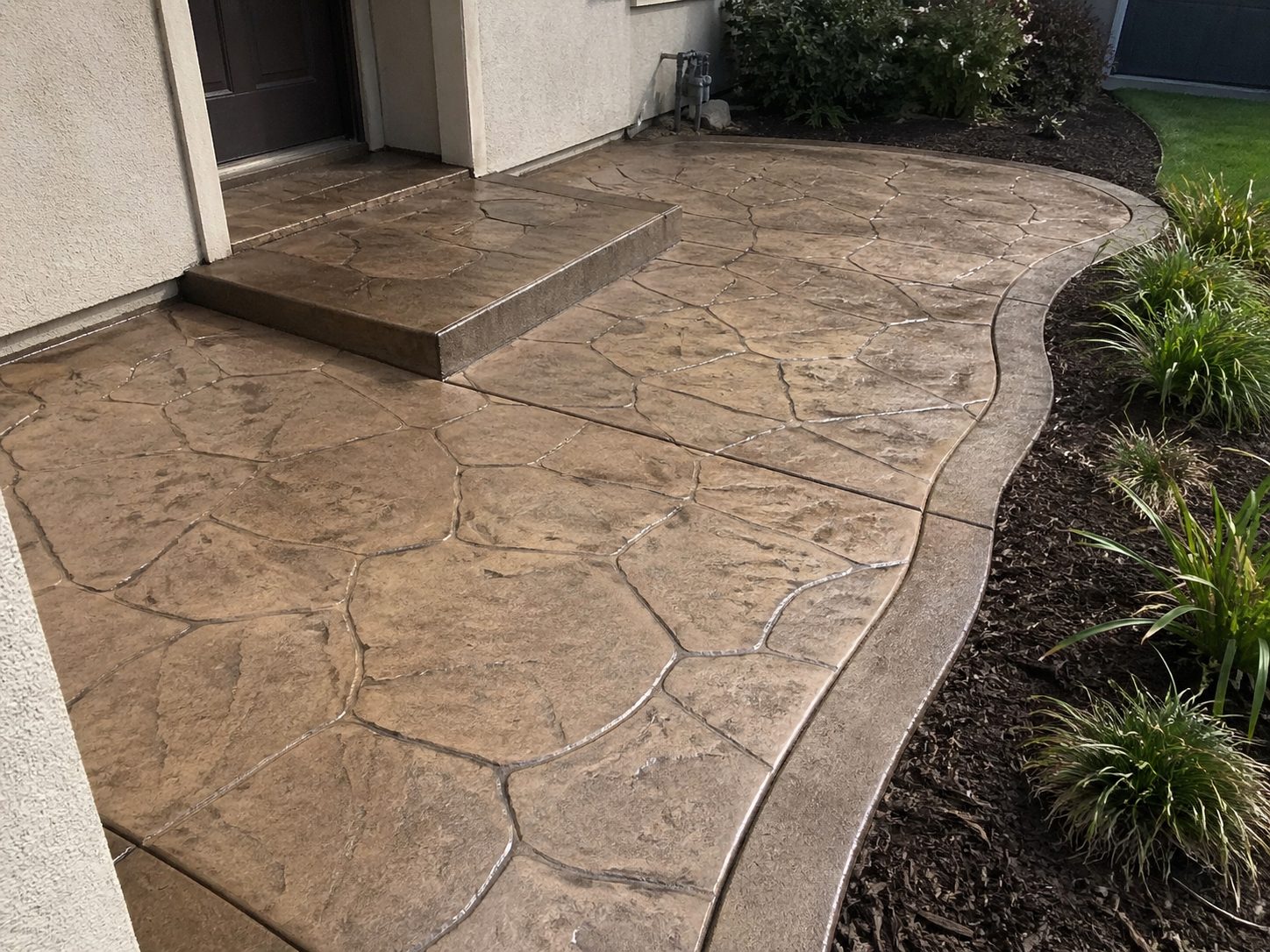 Finished stamped concrete entry walkway at a residential property — decorative stone pattern with landscaping