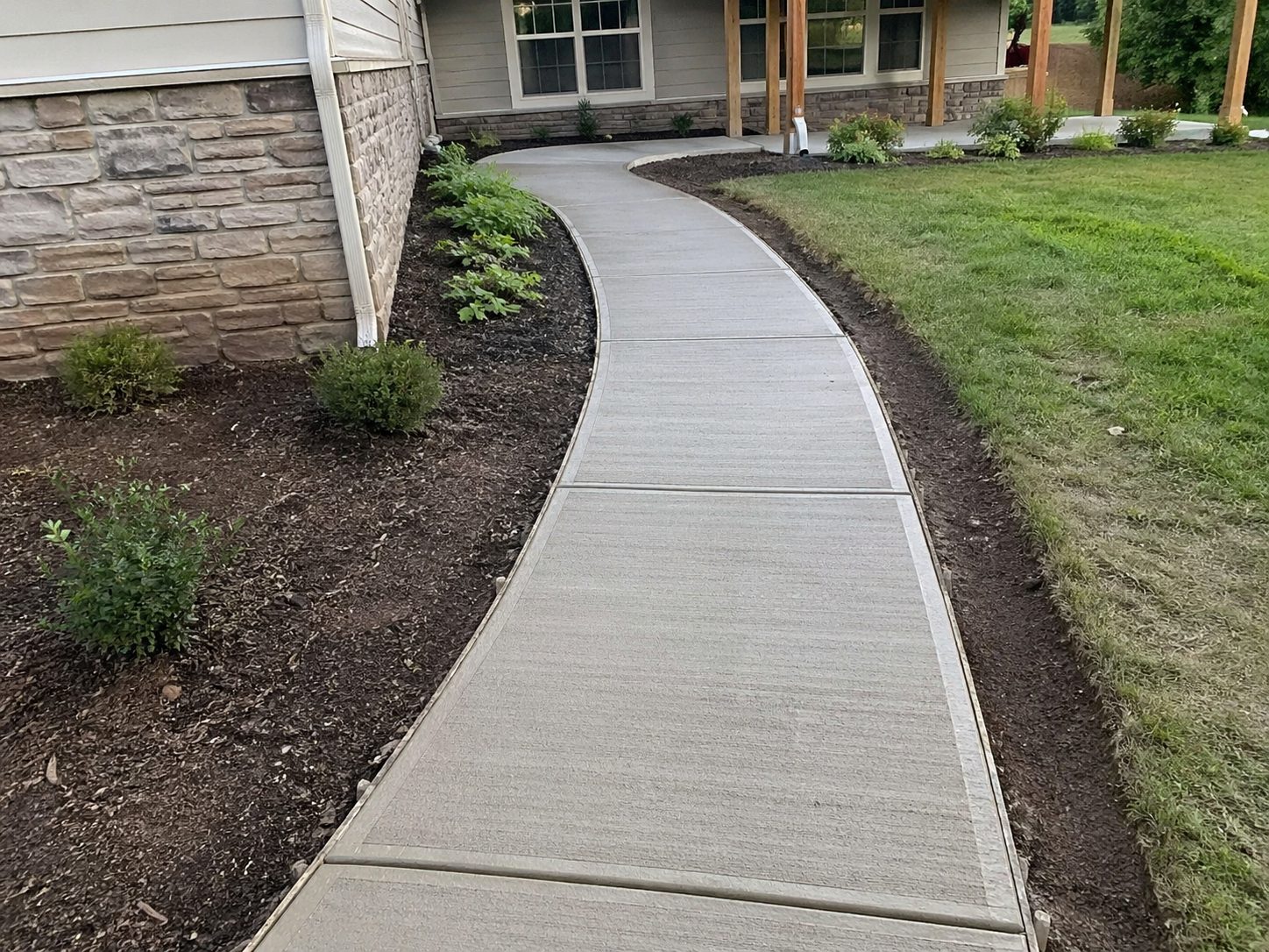 Finished curved concrete walkway at a residential property — clean installation with natural landscaping