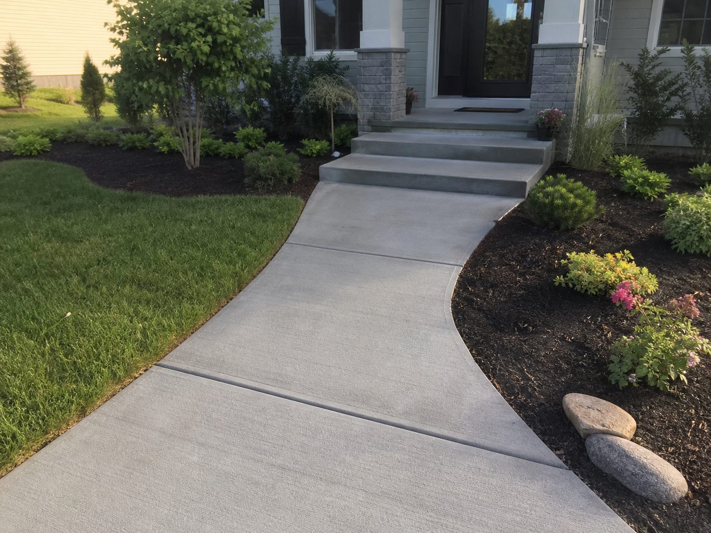 Finished concrete front walkway with steps and landscaping at a residential property